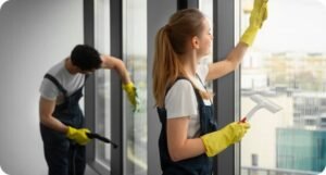 Zwei professionelle Gebäudereiniger reinigen große Fensterflächen – eine Person wischt mit einem Abzieher, die andere arbeitet mit Dampfreiniger, um streifenfreie und hygienische Ergebnisse zu erzielen.